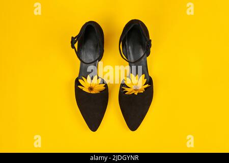 Suede black court shoes with yellow Topinambur flower bud inside toe on yellow background. Leather sandals with pointed toe and ankle strap made of bl Stock Photo