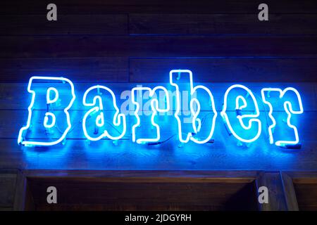 Blue neon wall sing with glowing barber inscription in loft barbershop interior. Retro LED neon text style on wooden wall on stylish barbershop recept Stock Photo