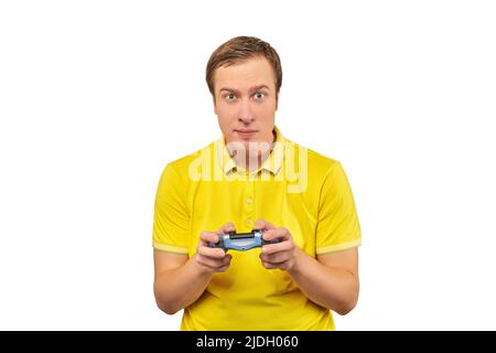 Funny attractive gamer in yellow T-shirt with gamepad isolated on white background. Cheerful young guy holding joy stick and playing videogames on TV, Stock Photo