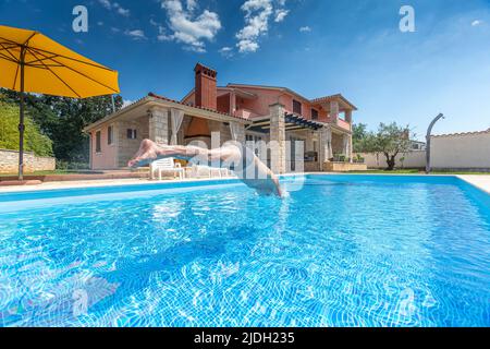 Croatia, Istria, Pula, senior man jumping into the pool in front of holiday house Stock Photo