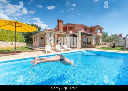 Croatia, Istria, Pula, senior man jumping into the pool in front of holiday house Stock Photo