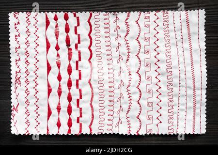 fabric with samples of stitches of sewing machine on dark wooden table Stock Photo