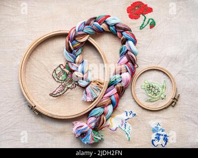top view of floss threads woven into braid and wooden hoops on fabric with embroideries Stock Photo