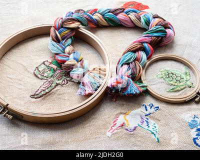 floss threads woven into braid and wooden hoops close up on fabric with embroideries Stock Photo
