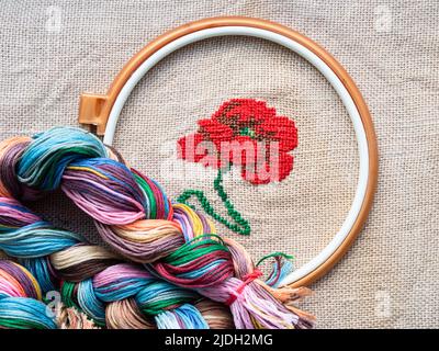 above view of mouline threads in braid, plastic hoop and red poppy flower embroidered by hand on fabric Stock Photo