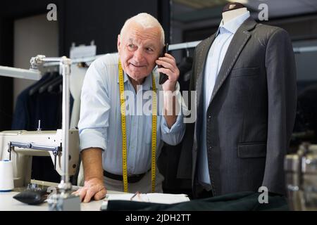Professional tailor man talking on mobile phone and making notes in notebook Stock Photo