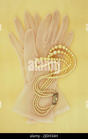 Pair of white nylon ladies see-through gloves lying on antique paper with triple-rowed set of pearls Stock Photo