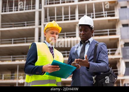 Engineer standing with builder supervising the construction process with house drawings on structure outdoors Stock Photo