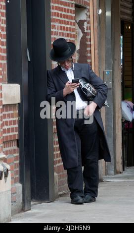 After morning services an orthodox Jewish man checks his cell phone for messages. He wouldn't have looked at it in the temple. In Williamsburg, Bklyn. Stock Photo