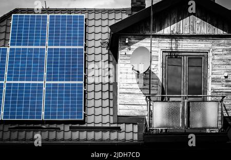 Solar panels on the roof of old wooden house with attic and small balcony, black and white image with selected blue colour Stock Photo