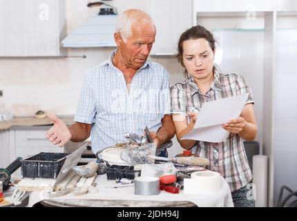 Perplexed woman and senior man with mixer tap and paper Stock Photo