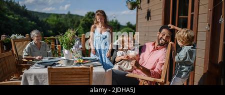 Three generation family having fun at barbecue party dinner on patio, people sitting at table on patio with grill. Stock Photo