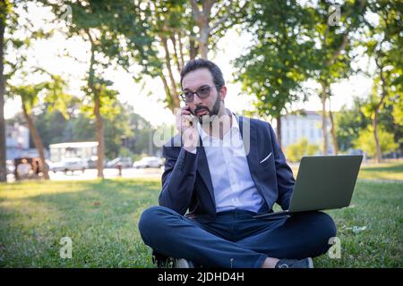 businessman makes a phone call while working with his laptop outside Stock Photo