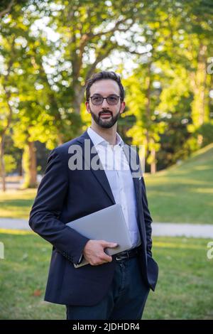portrait of a stylish caucasian businessman posing holding his laptop and looking away Stock Photo