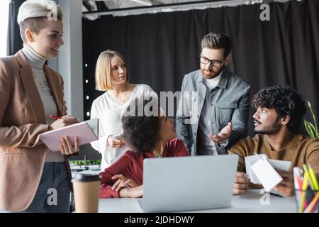 businessman in eyeglasses pointing with hand near multiethnic team working in ad agency Stock Photo
