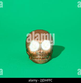 Brown skull with neon light eyes on green background. Spooky Halloween or Santa Muerte concept. Minimal horror idea. Stock Photo