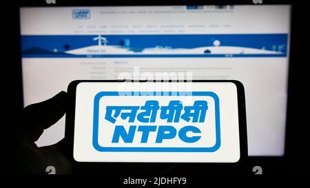 Person holding cellphone with logo of National Thermal Power Corporation Limited (NTPC) on screen in front of webpage. Focus on phone display. Stock Photo