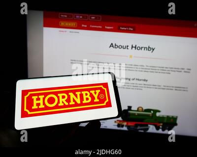 Person holding smartphone with logo of British model railway company Hornby plc on screen in front of website. Focus on phone display. Stock Photo