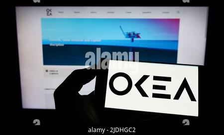 Person holding cellphone with logo of Norwegian oil company OKEA ASA on screen in front of business webpage. Focus on phone display. Stock Photo
