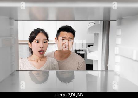 Shocked asian couple looking inside empty fridge at home Stock Photo