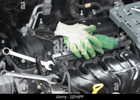 Wrenches and work gloves lie on the car engine in the engine compartment. Stock Photo