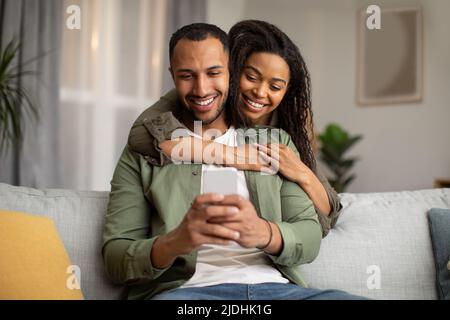 Happy African American Couple Using Mobile Phone At Home Stock Photo