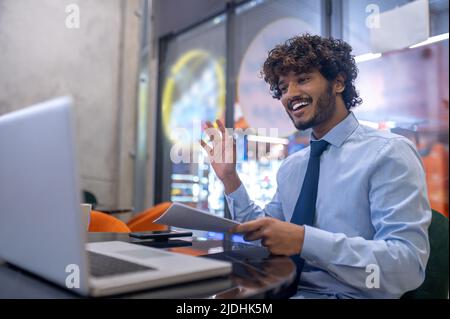 Man gesturing greeting looking at laptop sitting in office Stock Photo