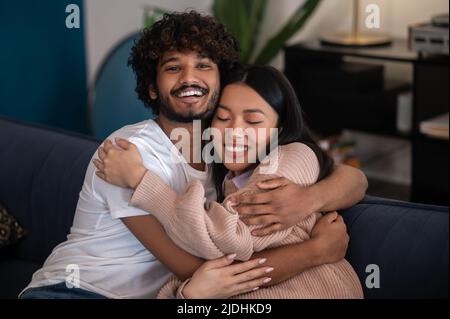 Handsome idnian guy hugging his asian girlfriend and both looking happy Stock Photo