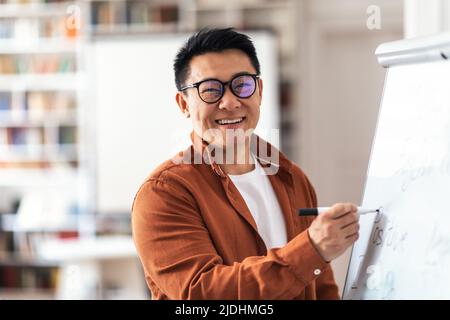 Positive Asian Teacher Man Smiling Writing On Whiteboard In Classroom Stock Photo