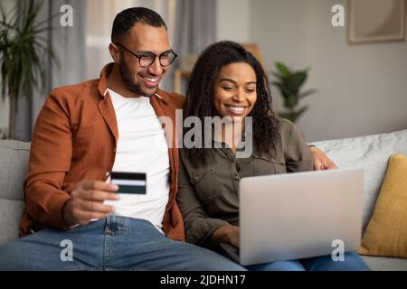 African Couple Shopping Online Via Laptop And Credit Card Indoor Stock Photo