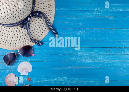 Flat lay composition with hat, sunglasses and seashells on a blue wooden background. Stock Photo