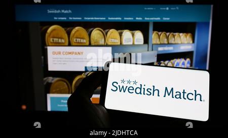 Person holding cellphone with logo of tobacco company Swedish Match AB on screen in front of business webpage. Focus on phone display. Stock Photo