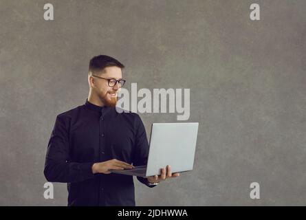 Cheerful smiling businessman working on laptop standing over studio background Stock Photo