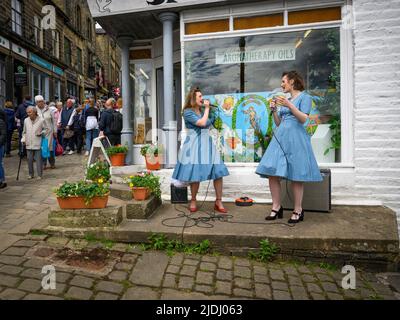 Haworth 1940 nostalgic retro living-history event (2 two ladies perform live music entertaining busy crowded Main Street) - West Yorkshire England UK. Stock Photo