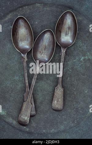 Three antique tarnished silver teaspoons lying on tarnished metal plate Stock Photo