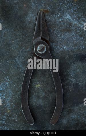 Vintage small pliers lying closed on tarnished metal sheet Stock Photo