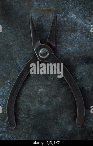 Vintage small pliers lying open on tarnished metal sheet Stock Photo