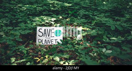 Poster with the inscription save the planet in the forest among the plants. Stock Photo