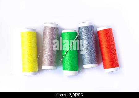 Set of colorful spools of sewing threads with needle, seamstress tools isolated on white background. Stock Photo