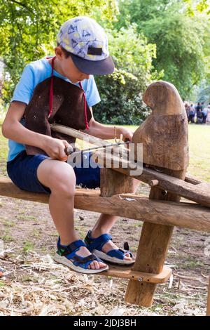 Boy child kid shaving branch of wood with traditional tools at Tunderfesztival 2022, Sopron, Hungary Stock Photo