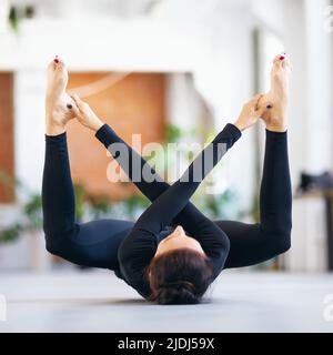 Woman in black sportswear practicing yoga doing supta rudrasana exercise, exercising while lying on a mat in the room Stock Photo