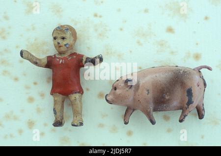 Worn lead models of Victorian toddler with arms outstretched and jaunty plump pig lying on antique paper Stock Photo