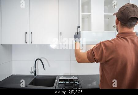Handyman Checking the Doors on a Freshly Installed Wall Mounted Kitchen Storage Cabinet Combination Making Sure the Job Was Done Right. Stock Photo