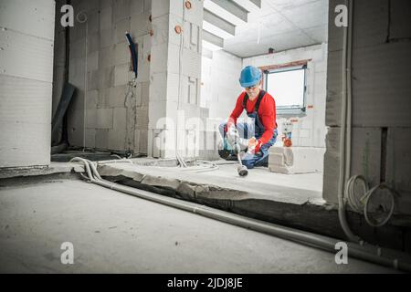 Caucasian Construction Worker in Safety Helmet and Glasses Doing His Job Using Hole Saw Blade Attachment with His Power Drill. Construction Site Backg Stock Photo