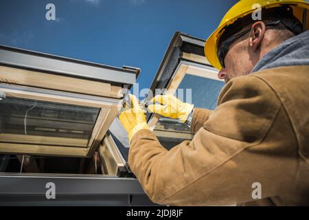 Caucasian Worker Wearing Safety Helmet and Protective Gloves Carrying Out Repair Works on Roof Skylight Windows Using His Screwdriver. Stock Photo