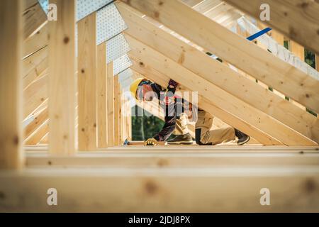 Building Process of the Roof Wooden Skeleton in the New Residential House. Caucasian Worker Driving the Nails Into Beams Using His Claw Hammer Constru Stock Photo