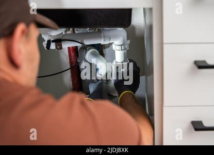 Professional Caucasian Plumber Installing New Sink Drainage in a Residential Kitchen Cabinet Stock Photo