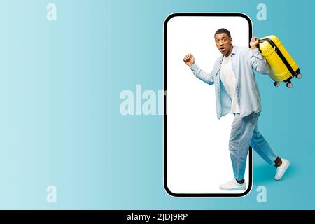 Excited African-American guy carrying yellow suitcase running inside huge mobile phone, scared multiracial man fears does not take advantage of a good offer, hurrying. App for travelers Stock Photo