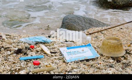 Used reusable face mask with Covid test, plastic bottle and other trash lies on the beach Stock Photo