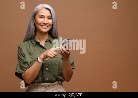 Happy business woman touching to the smartphone screen while feeling great with new phone features. Indoor studio shot isolated on brown background Stock Photo